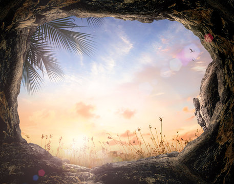 Easter Sunday concept: Empty tomb stone with palm leaves over meadow sunset background