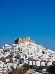 Fototapeta na wymiar Chora of Astypapaia island ,Greece at daytime with the white houses that encircle the castle and the white windmills with the red roofs.