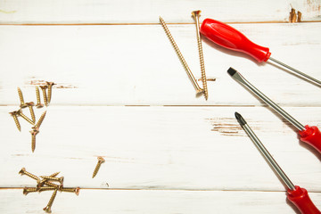 Repair carpenter tools: red screwdrivers and screws on white old wooden background, top view, copy space