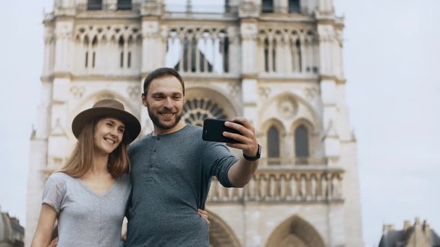 Happy young woman standing near the Notre Dame in Paris, France and taking selfie photos on smartphone.