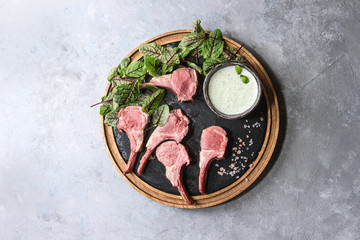 Grilled sliced rack of lamb with yogurt mint sauce served with green salad young beetroot leaves and pink salt on round wooden slate board over grey texture background. Top view, space © Natasha Breen