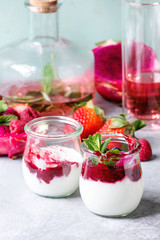Jars of natural white yogurt with berry sauce, fruit salad with pink dragon fruit, berries and mint, served with bottle of lemonade on grey table. Close up. Healthy eating