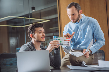 creative designers picking color from palette together at office