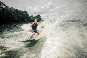 Young and athletic man wakesurfing on the board against the sky