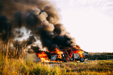 Naklejka premium Car burning with open flames and black smoke on a field