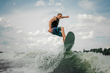 Young and athletic guy wakesurfing on the board down the river - obrazy, fototapety, plakaty