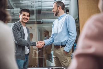 Obraz premium smiling business colleagues shaking hands at modern office