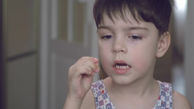 The boy tries to pull out his milk tooth with a thread.