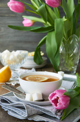 Pink tulips and a cup of green tea with lemon on a tray