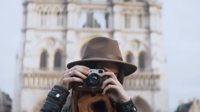 Young beautiful woman standing near the Notre Dame in Paris, France and taking photos on retro film camera.