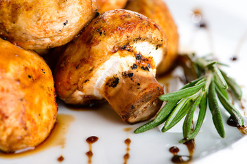 Delicious appetizing baked mushrooms with sauce in a white plate on dark background. Food background