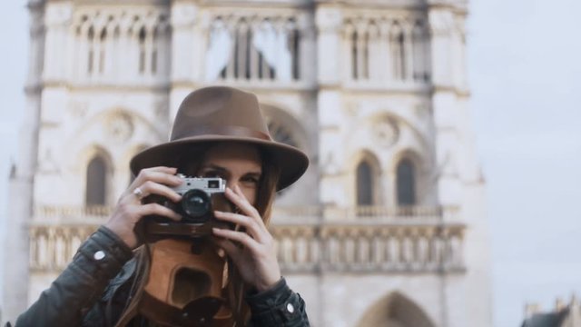 Portrait of young smiling woman standing near the Notre Dame cathedral and taking photos on film camera in Paris, France