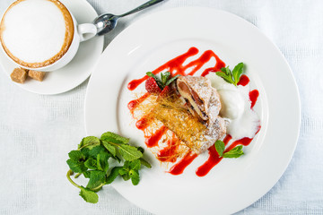 Delicious sweet strawberry strudel with candy sprinkles, mint and ice-cream in a white plate. Top view, flat lay