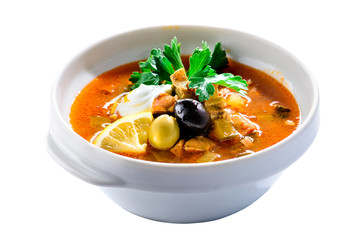 Delicious soup saltwort (Solyanka) with lemon, meat, pickles, tomato sauce and olives on a white plate