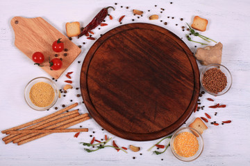 Food frame around brown round cutting board on white wooden table.