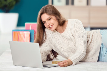 Young woman shopping online with credit card and laptop on floor