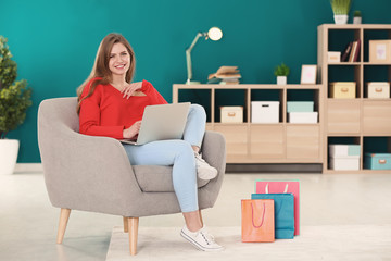 Young woman shopping online with laptop in armchair