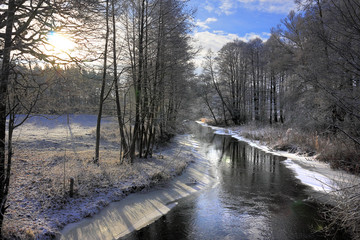 Winter landscape of woods and river covered with ice and snow in Masuria lakes district in Poland -...