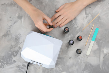 Woman making manicure near ultraviolet lamp on table