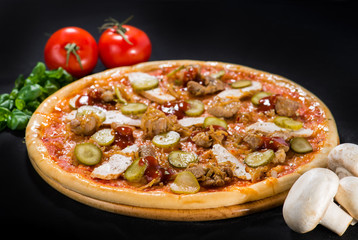 Appetizing pizza with salami, mozzarella, pepper, meat and pickled cucumbers on wooden board on dark background