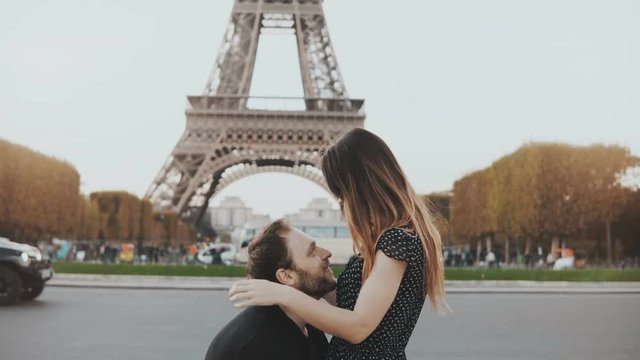 Young happy couple walking, kissing near the Eiffel tower in Paris, France. Traveling man and woman on honeymoon.