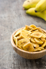 Banana chips in wooden bowl on wooden table background