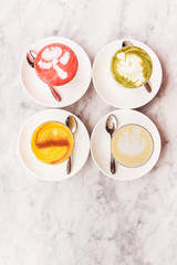 Four different colored latte coffee, style of foam art, natural organic beverages in modern cafe on white marble background