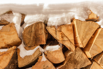 Pile of stacked chopped firewood covered with snow, close up