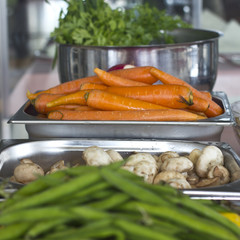 Fresh vegetables in metal trays in the restaurant. Carrots, green string beans, champignons
