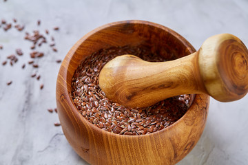 Top view close-up picture of wooden pestle and mortar with flaxseeds on light background, shallow depth of field