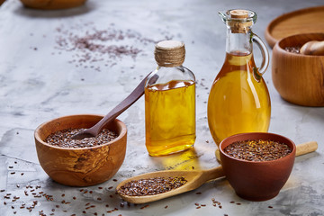 Flax seeds in bowl and flaxseed oil in glass bottle on light textured background, top view, close-up, selective focus