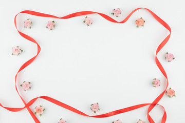 Pink and orange paper flowers and red ribbon on white background with copy space