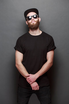 Hipster handsome male model with beard wearing black blank t-shirt with space for your logo or design over gray background