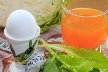 Boiled egg on a stand, fresh cabbage, salad, ruler and glass of multivitamin juice