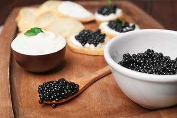 Fototapeta na wymiar Bowl and spoon with delicious black caviar on wooden board