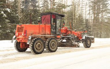 Winter. Snowing. The tractor clears the snow from the road.