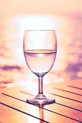 Silhouette glass of wine on a wooden table with  seascape and skyline in the evening with sunset tone style.