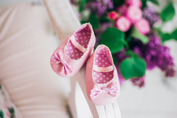 Closeup top view of pair of small sweet new pink shoes for little infant on sofa in home interior. Blurry colorful flowers in background. Happy expectation of new baby girl concept.