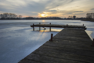 Obraz na płótnie Canvas Wooden jetty and frozen lake at sunset