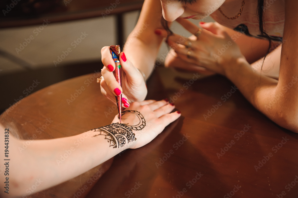 Wall mural Master mehndi draws henna on a female hand.