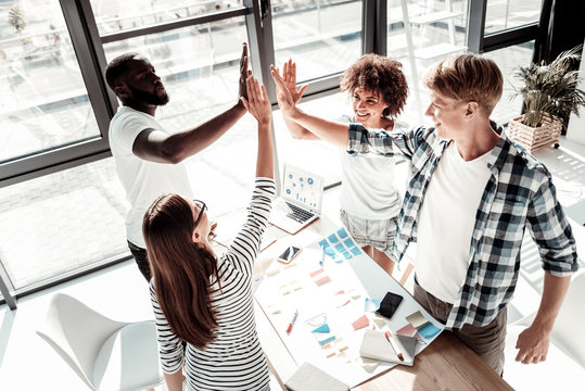 Best Team. Cheerful Delighted Positive People Standing Around The Table And Giving Each Other High Five While Working In Team