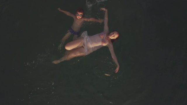 Aerial shot of a mother with son swimming the sea then distant view from copter flying higher
