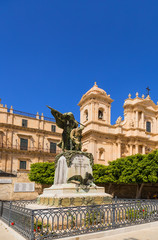 Fototapeta na wymiar Noto, Sicily, Italy. Monument to the inhabitants of Noto, who died during the First World War, against the backdrop of the Palazzo Landolina and the Cathedral
