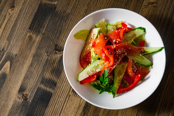 Salad with smoked salmon and cucumber, tomato, pepper in bowl on a wooden background
