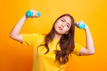 Exhausted Asian woman with dumbbells in yellow dress