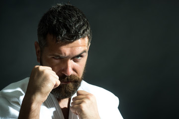 Karate man in a kimono hits a hand on dark background. Male shows judo or karate in white kimono. Handsome male karate shows a punch. Karate man is preparing for the competition. Copy space.