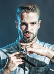 Stylish hairdresser with dangerous razor for shaving in studio. Portrait brutal caucasian hipster, unshaven man with vintage straight razor. Sexy macho demonstrating sharp blade of his dangerous razor
