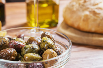 Glass bowl with different kind of olives and and fresh bread ciabatta on wooden table.
