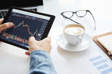 Young trader is sitting in home at table, working on tablet with graphs,diagrams on monitor. Crypto currencies, trader using tablet and computers