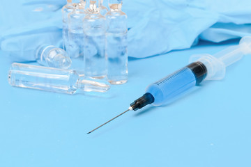 Medicaments in ampoules, medical syringe, medical gloves, on a blue background, soft focus